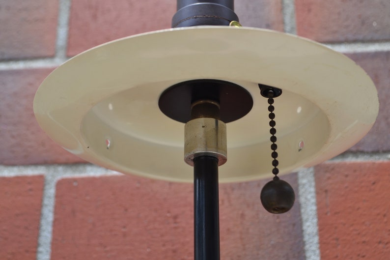 May include: A white ceiling lamp with a black metal base and a pull chain. The lamp has a round, flat shade.
