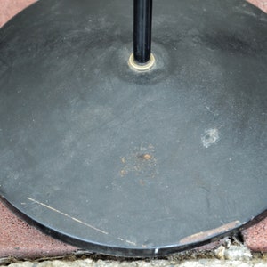 May include: Black round base for a floor lamp. The base has a metal finish and a slightly textured surface.
