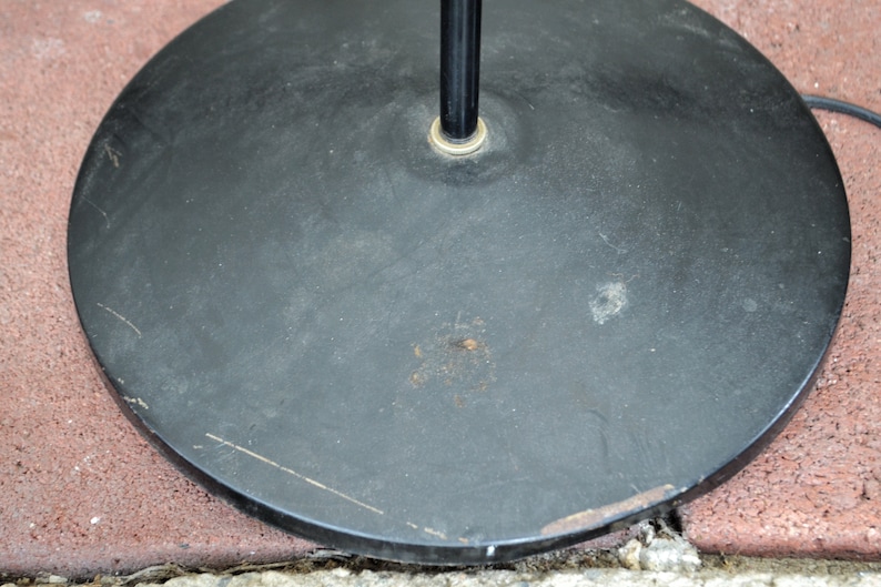 May include: Black round base for a floor lamp. The base has a metal finish and a slightly textured surface.