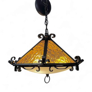 May include: A black wrought iron chandelier with a square, amber glass shade and a frosted glass diffuser. The chandelier has a decorative chain and a circular ceiling mount.
