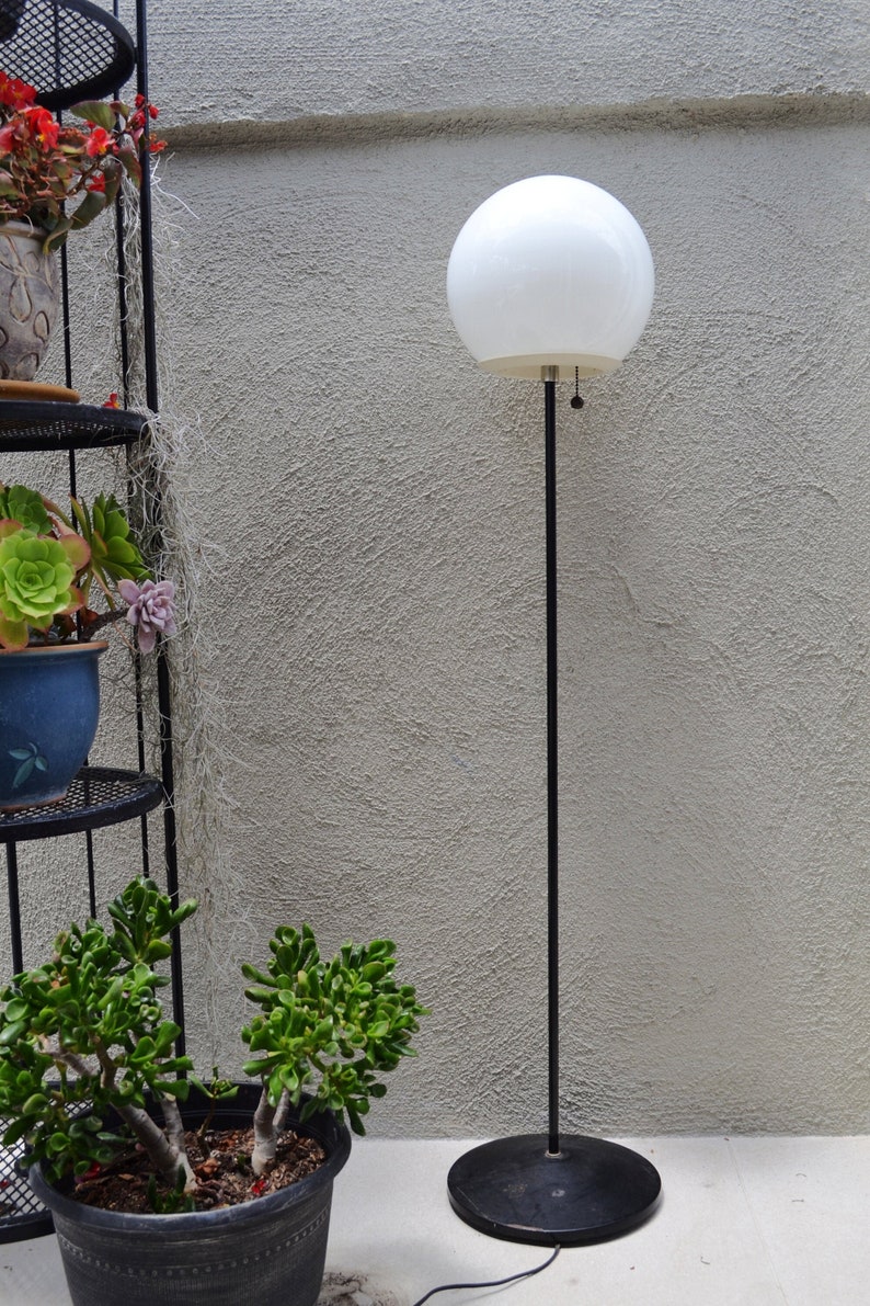 Vintage glass orb mid century atomic style floor lamp black and white with potted succulents and a stucco wall.