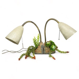 May include: A pair of vintage brass lamps with beige shades, mounted on a brick planter with green succulents.