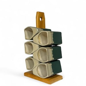 Peut inclure: Porte-bouteilles en céramique empilé avec six compartiments. Le support est composé de compartiments rectangulaires beiges et vert foncé, avec une base et une poignée en bois. Les compartiments sont disposés en quinconce, et la poignée a un trou.