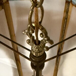 Close up view of the hardware on a vintage swag lamp with hexagonal shape and oval cutout, hanging on chain against a white background.