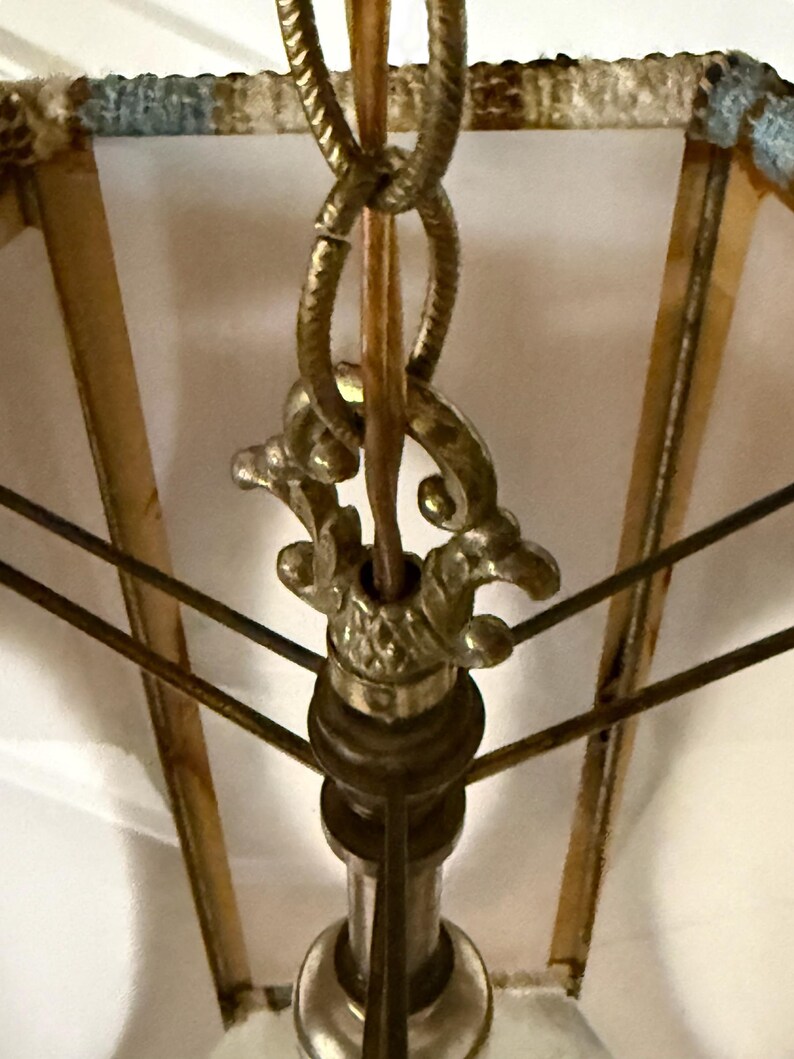 Close up view of the hardware on a vintage swag lamp with hexagonal shape and oval cutout, hanging on chain against a white background.