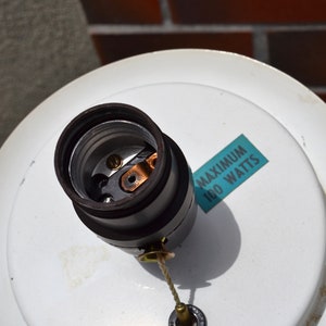 May include: A white ceiling fixture with a black electrical socket and a blue label that reads "MAXIMUM 100 WATTS".