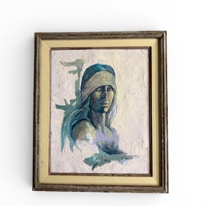 May include: Oil painting portrait of a woman with a blue head covering and long hair, framed in a wooden frame. The artwork features a textured, impasto style with shades of blue, white, and gold. The woman's face is the focal point.