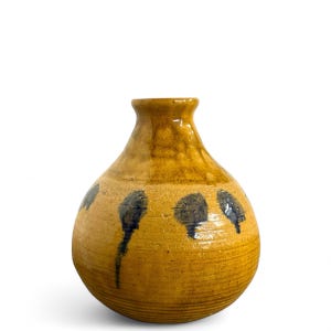 May include: A handcrafted, ceramic vase with a bulbous body and a narrow neck. The vase is primarily a warm, mustard yellow color, with dark blue, abstract painted accents. The vase has a textured surface and a glossy finish.