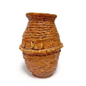 May include: A brown ceramic vase with a textured surface and a band of decorative swirls around the middle.