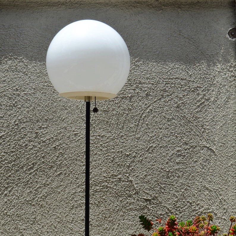 Vintage glass orb mid century atomic style floor lamp black and white with potted succulents and a stucco wall.