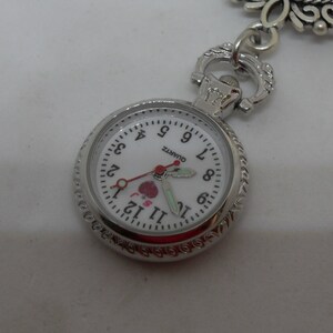 May include: A silver pocket watch with a white face and black numbers. The watch has a small red heart with the words "I love you" on it. The watch is on a white background.