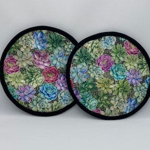 Puede incluir: Dos posavasos redondos de tela negra y blanca con un patrón de suculentas. Los posavasos están hechos de una tela suave acolchada y tienen un borde negro.