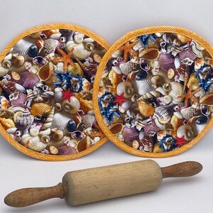 May include: Two round, seashell-themed pot holders with a yellow border and a wooden rolling pin. The pot holders are filled with various seashells, starfish, and coral in shades of white, beige, red, and blue.