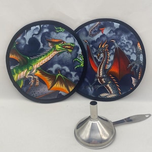 May include: Two round fabric trivets with dragon illustrations, one green and one red, set against a dark blue cloudy background. A silver metal funnel with a handle is in the foreground.