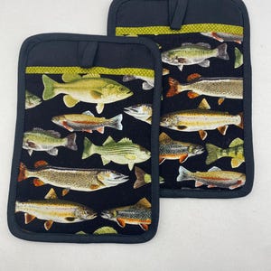 May include: Two black pot holders with a green trim and a pattern of colourful fish on a black background.