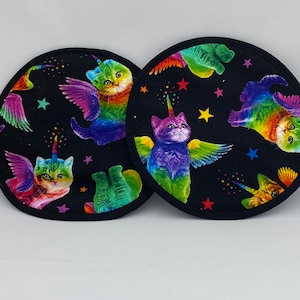 Puede incluir: Dos posavasos redondos negros con un diseño de gato unicornio arcoíris. Los gatos tienen alas y están rodeados de estrellas.