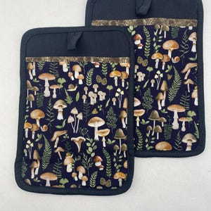 May include: Two black pot holders with a brown trim and a mushroom and leaf pattern on a dark blue background.