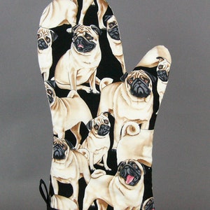 May include: A beige oven mitt with a black background, featuring a repeating pattern of pug dogs. The pugs have black faces and are in various poses. The mitt has a black loop for hanging.
