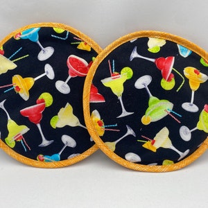 May include: Two round black and yellow pot holders with a pattern of colorful cocktails on a black background.