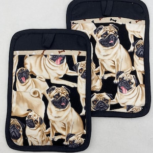 May include: Two black oven gloves with a pug dog pattern. The gloves have a black border and a loop for hanging. The pug pattern features various pug dog poses on a black background.
