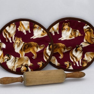 Puede incluir: Dos posavasos redondos marrones con fondo burdeos y un patrón de perros Collie marrones y blancos. Un rodillo de madera está en primer plano.