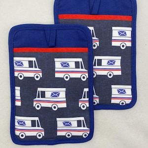 Puede incluir: Dos agarradores rectangulares con fondo de tela azul oscuro y un patrón repetitivo de camiones de correo blancos. Cada camión tiene rayas rojas y azules y un icono de sobre azul. Los agarradores tienen un borde azul y una trabilla para colgar.