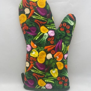 May include: A dark green oven mitt with a colorful vegetable pattern. The design includes illustrations of tomatoes, carrots, eggplants, peppers, onions, and other vegetables. The mitt is designed for kitchen use.