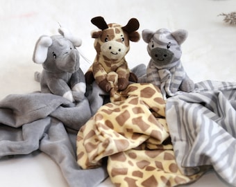 Puede incluir: Tres mantas de bebé de peluche con animales. Un elefante gris, una jirafa marrón y una cebra gris y blanca. Cada animal está unido a una manta con el estampado del mismo animal.