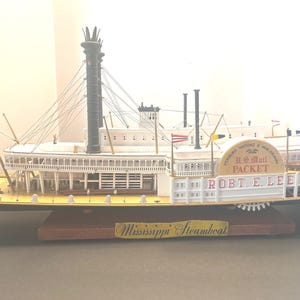 May include: A detailed model of the steamboat "ROBT. E. LEE" with a yellow and white exterior. The model features a paddle wheel, smokestacks, and American flags. The words "U.S. Mail Packet" and "Mississippi Steamboat" are visible.