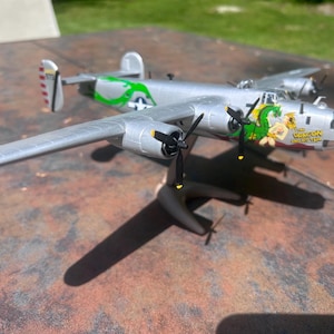 May include: A silver model airplane with black propellers and a green dragon graphic on the side. The model has a detailed design, including wings, tail, and a stand. The text "The Oregon Raider" is visible on the plane.