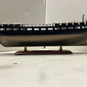 May include: A black wooden model ship with white sails on a wooden base. The ship has a detailed hull and rigging.