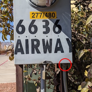 May include: A white metal box with a black number "6636" and the word "AIRWAY" printed on it. The box has a yellow sticker with the text "277/480". A metal padlock is attached to the box.