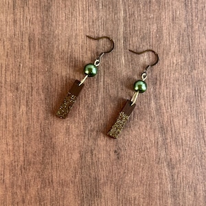 May include: A pair of earrings with a dark brown wooden bar and a green pearl bead on each earring.