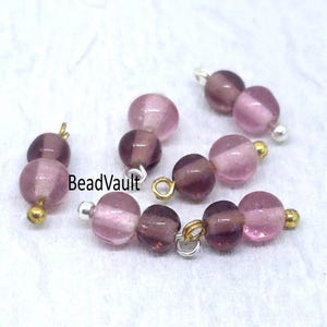 May include: Several strands of purple and pink glass beads with gold and silver findings. The beads are round and have a translucent quality. The image is on a white background.