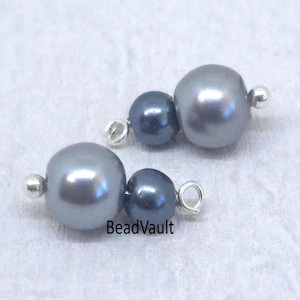 May include: Two sets of gray and dark blue pearl beads with silver findings. Each set has a large gray pearl, a smaller dark blue pearl, and a silver loop. The beads are on a white surface. The text "BeadVault" is visible.