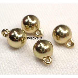 May include: Four gold-colored, spherical jewelry components with small loops attached. The components are shiny and reflective, with a smooth surface. The text "BeadVault" is visible on the image.