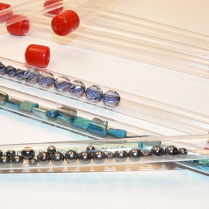 May include: Six clear plastic tubes with red caps, filled with various small beads and metal balls. The tubes are arranged in a row on a white surface.