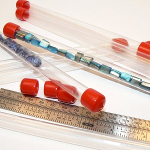 May include: A set of clear plastic tubes with red caps, filled with various blue and green beads. A ruler is also visible in the image.
