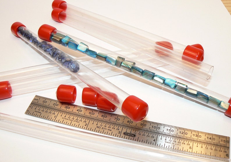 May include: A set of clear plastic tubes with red caps, filled with various blue and green beads. A ruler is also visible in the image.