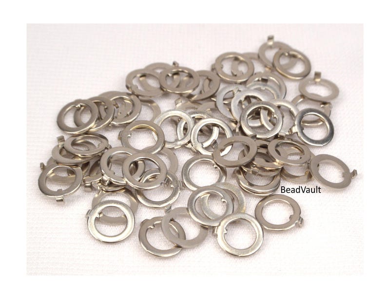 May include: A large quantity of silver jump rings, a type of jewelry finding, are scattered on a white surface. The jump rings are all the same size and are made of metal.