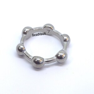 May include: A silver-colored ring with a unique design. The ring features a series of rounded, ball-like shapes connected in a circular pattern. The text "BeadVault" and the number "7" are visible on the ring.