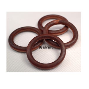 May include: Four brown wooden rings, each with a smooth, rounded surface. The rings are stacked on top of each other, with the largest ring at the bottom and the smallest ring at the top. The rings are all made of the same type of wood, and they have a natural, rustic look.