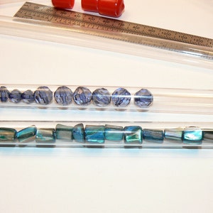 May include: Two clear plastic tubes with red caps filled with blue and green beads. The tubes are on a white surface.