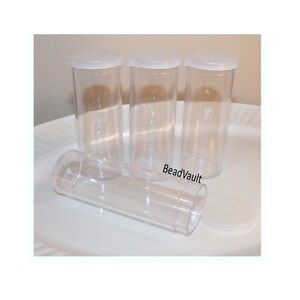 May include: Four clear cylindrical plastic storage containers with matching translucent white snap-on lids. Three of the containers are standing upright in a row, while one container lies horizontally in the foreground with its lid detached.