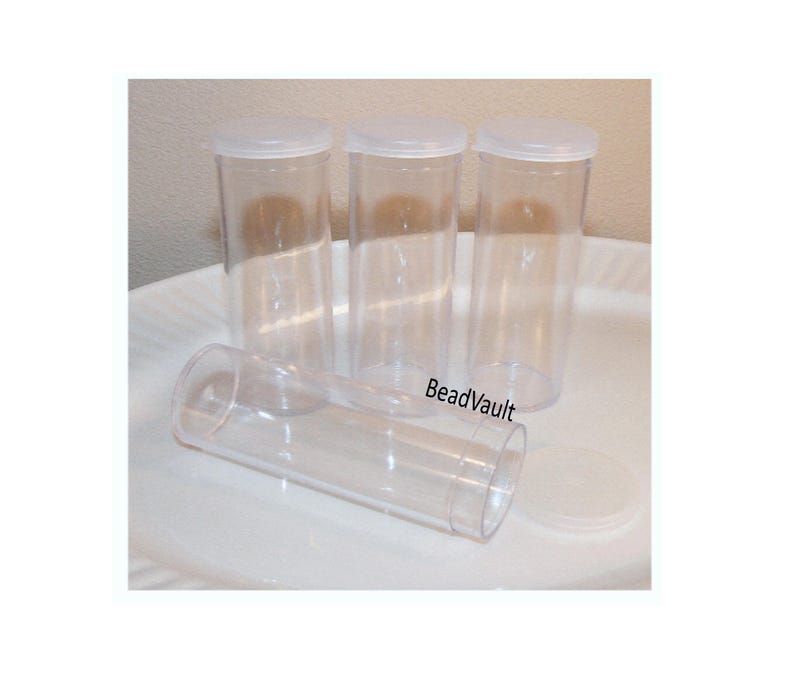 May include: Four clear cylindrical plastic storage containers with matching translucent white snap-on lids. Three of the containers are standing upright in a row, while one container lies horizontally in the foreground with its lid detached.