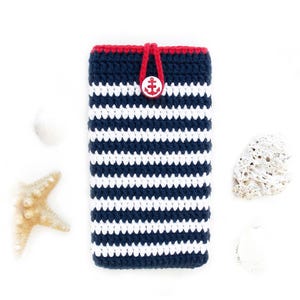 May include: A rectangular crochet phone pouch featuring horizontal navy blue and white stripes. The top edge is trimmed in red yarn with a matching red loop closure secured by a white button embossed with a red anchor design.