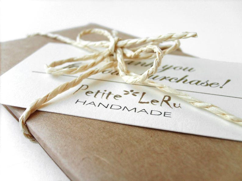 Puede incluir: Un paquete de papel marr&oacute;n envuelto con una cuerda de rafia de color beige claro atada en un lazo. Una tarjeta rectangular blanca est&aacute; metida bajo la cuerda, con el texto impreso "Thank you for your purchase!" y la marca "Petite LeRu HANDMADE".