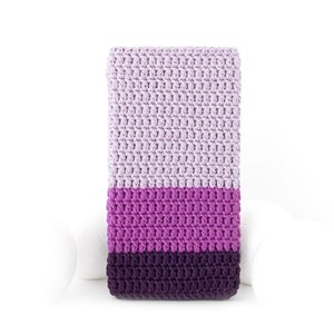 May include: A rectangular, crocheted item in shades of lavender, purple, and deep violet. The handmade piece features a striped color block design, with each section of color clearly defined. The texture of the crochet stitches is visible.