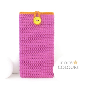 May include: A rectangular crochet phone pouch in bright pink with an orange top border. It features a yellow button closure with an orange loop. The text "more COLOURS" with a small flower icon is visible in the lower right corner of the image.