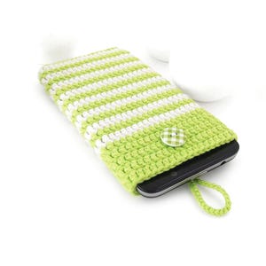 Puede incluir: Una funda de ganchillo para tel&eacute;fono con rayas verde lima y blancas, que presenta una solapa verde lima lisa asegurada por un peque&ntilde;o bot&oacute;n a cuadros verde y blanco. Un lazo trenzado verde lima a juego sobresale de la base de la funda.